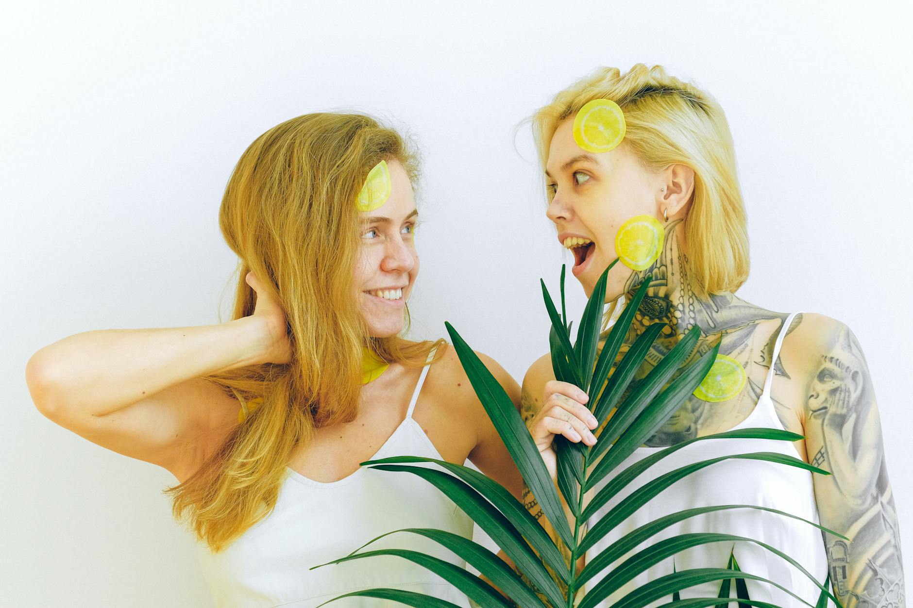 Two women smiling with joy, holding lemons and tropical plants indoors, symbolizing freshness and reconnection