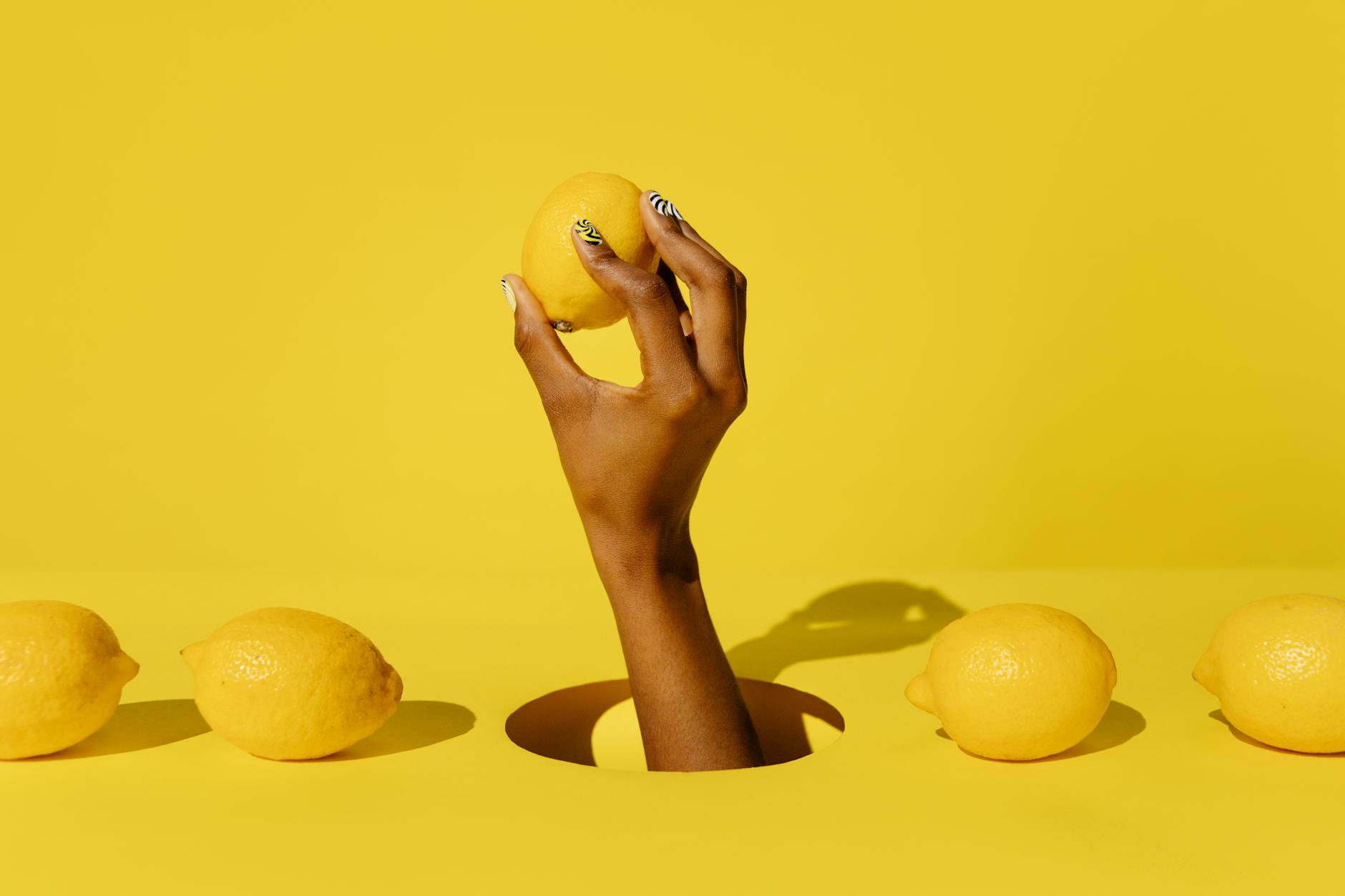 Hand holding a fresh lemon against bright yellow background, symbolizing simplicity and natural pleasure