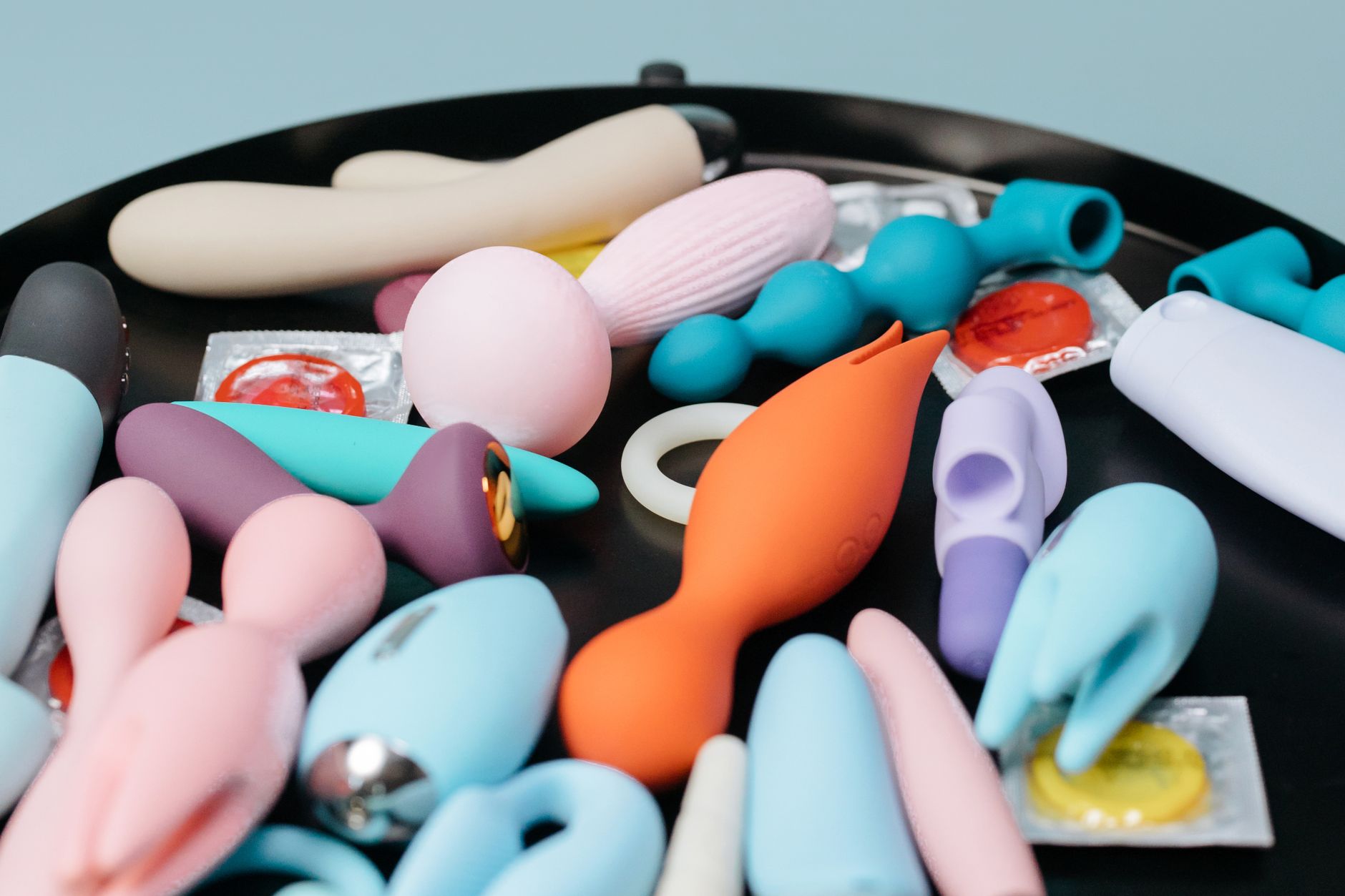 A vibrant collection of various sex toys on a black tray, featuring diverse shapes and colors including clitoral vibrators