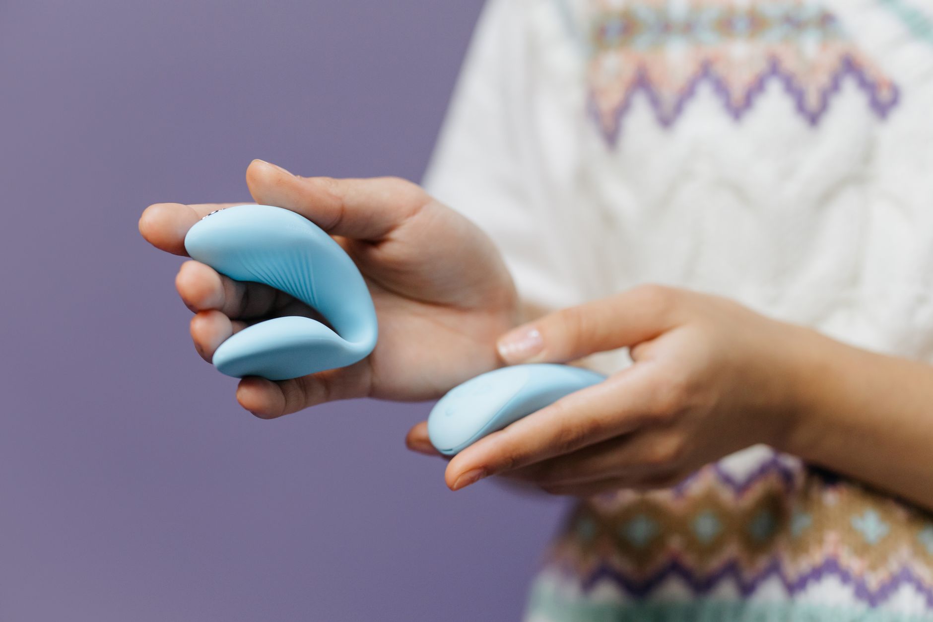 Intimate close-up of hands holding a sleek lemon vibrator against a purple background.