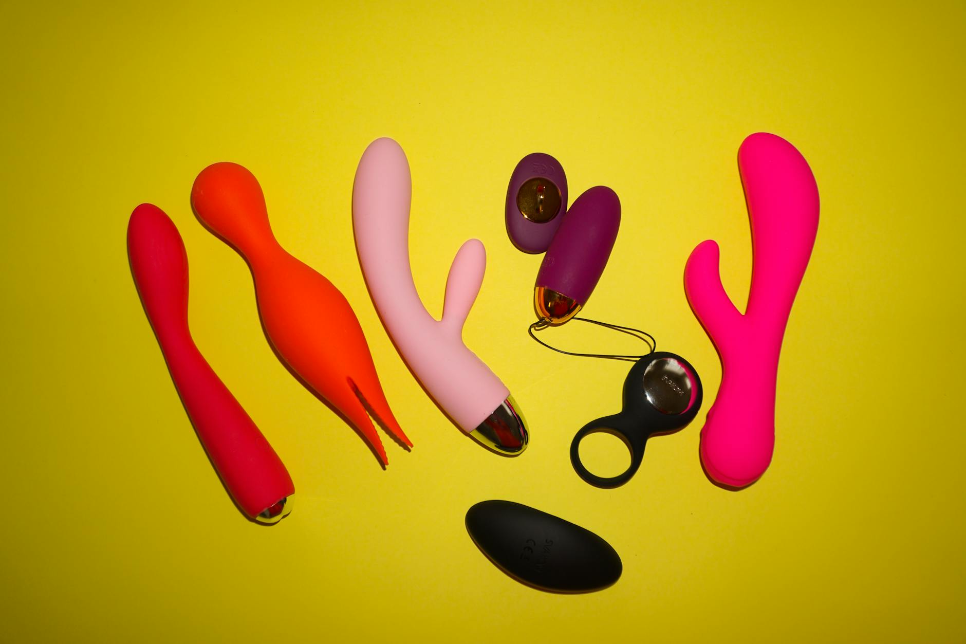 Collection of colorful vibrators and adult toys arranged on a bright yellow background